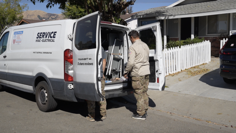 HVAC technicians unloading tools from a service van outside a residential home in California.
